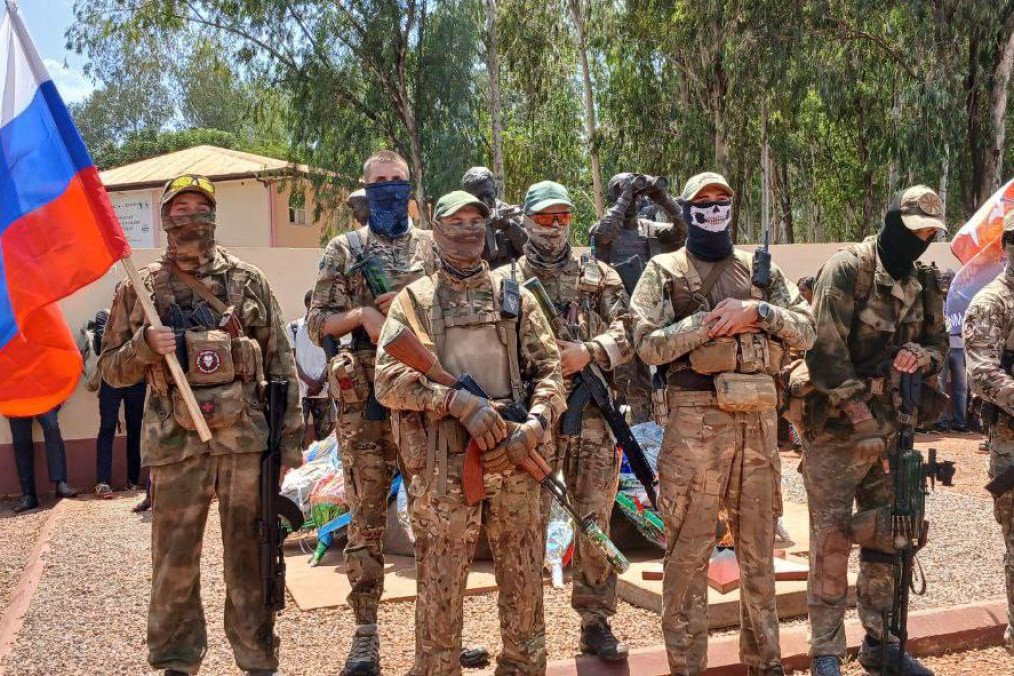 Africa Corps soldiers posing with a Russian flag in Africa, representing the continued Russian military presence after Wagner's nominal withdrawal