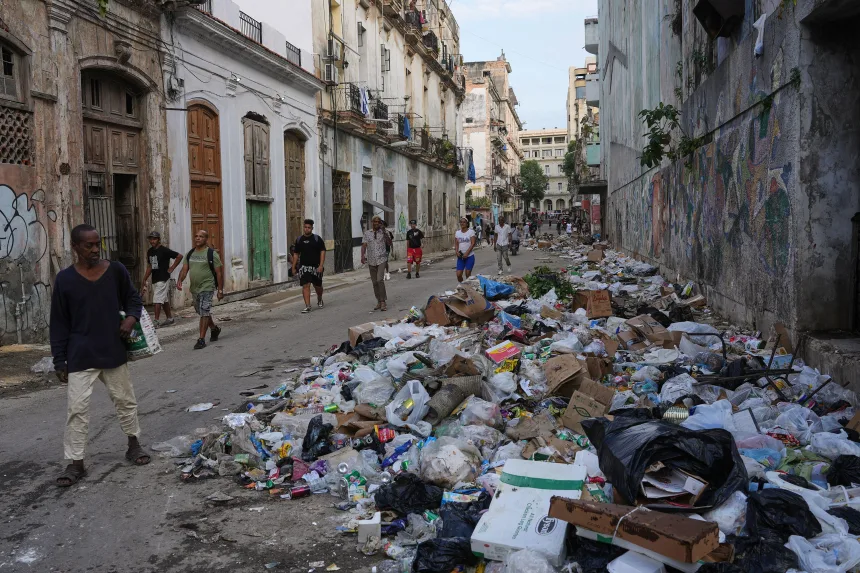People walking past piles of uncollected trash on a street in Havana during the 2026 economic crisis
